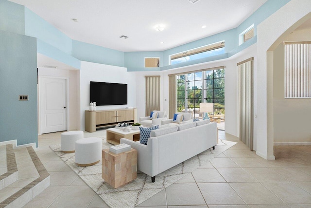 living room featuring a high ceiling, visible vents, light tile patterned floors, arched walkways, and baseboards