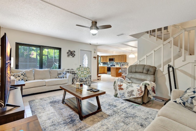 living room with a textured ceiling, a ceiling fan, visible vents, and stairway