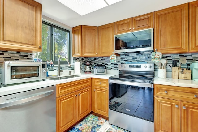 kitchen featuring light countertops, backsplash, light tile patterned flooring, appliances with stainless steel finishes, and a sink