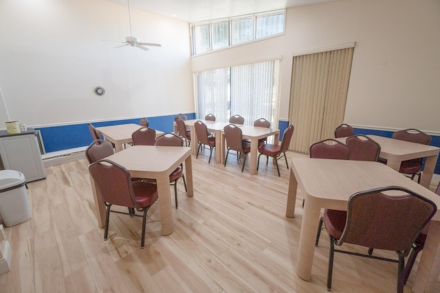 dining space with a ceiling fan, light wood finished floors, and a towering ceiling