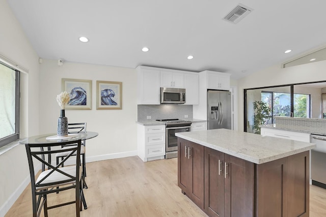 kitchen featuring visible vents, a center island, tasteful backsplash, light wood finished floors, and appliances with stainless steel finishes