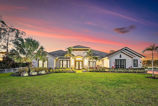 view of front of home featuring french doors, stucco siding, fence, and a yard