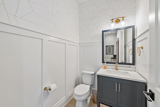 bathroom with toilet, a decorative wall, and vanity