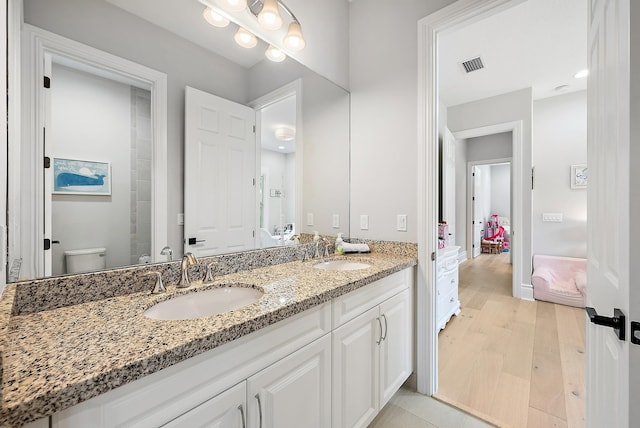 ensuite bathroom featuring double vanity, visible vents, a sink, and wood finished floors