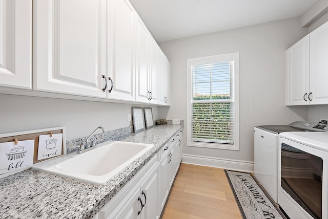 laundry room featuring baseboards, a sink, light wood finished floors, cabinet space, and washer and clothes dryer