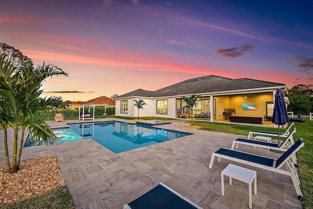 pool at dusk with a patio area, ceiling fan, a lawn, and an outdoor pool