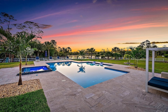 pool at dusk with a yard, fence, a pool with connected hot tub, and a patio