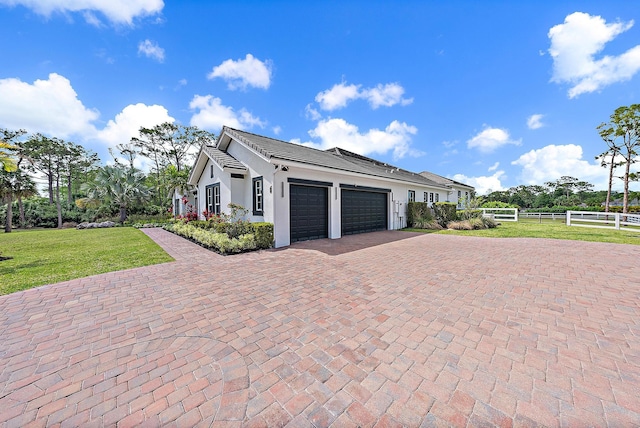 view of side of home featuring stucco siding, a lawn, decorative driveway, fence, and an attached garage