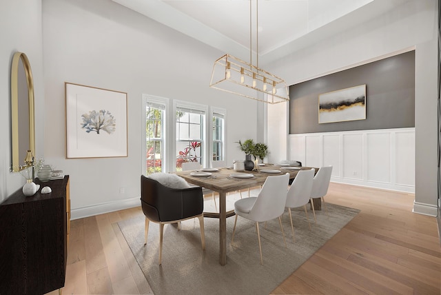 dining area featuring baseboards, an inviting chandelier, a decorative wall, hardwood / wood-style flooring, and a towering ceiling