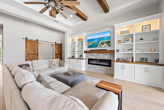 living area with built in features, ceiling fan, light wood-type flooring, a glass covered fireplace, and a barn door