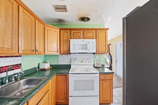 kitchen with white appliances, visible vents, a sink, and decorative backsplash