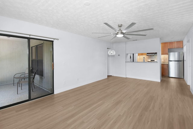 6551 SE Federal Hwy Unit 203, Stuart, FL 34997 - unfurnished living room featuring light wood-style floors, baseboards, a ceiling fan, and a textured ceiling