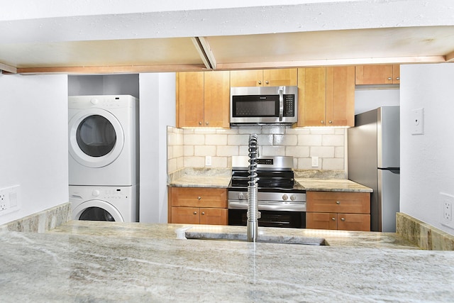 6551 SE Federal Hwy Unit 203, Stuart, FL 34997 - kitchen featuring backsplash, light stone countertops, stacked washer / dryer, brown cabinetry, and appliances with stainless steel finishes