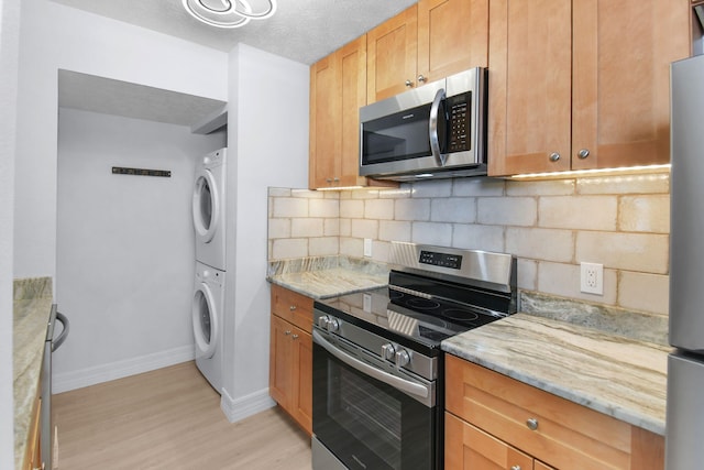 6551 SE Federal Hwy Unit 203, Stuart, FL 34997 - kitchen featuring appliances with stainless steel finishes, light wood finished floors, backsplash, and stacked washer / drying machine