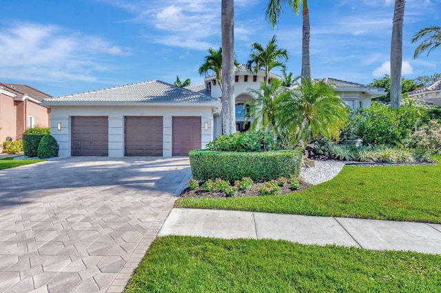 mediterranean / spanish-style home with a tiled roof, stucco siding, a front lawn, an attached garage, and driveway