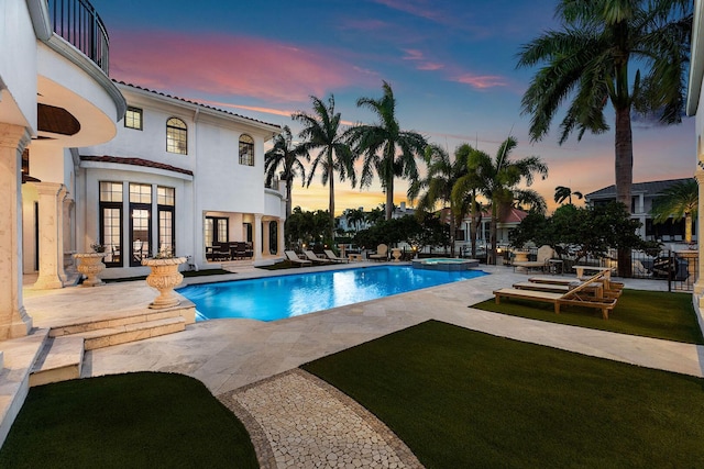 251 W Coconut Palm Rd, Boca Raton, FL 33432 - pool at dusk featuring a lawn, a pool with connected hot tub, french doors, and a patio area