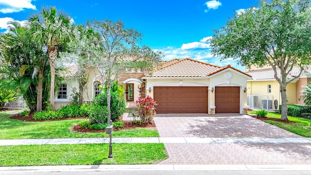 mediterranean / spanish-style home featuring a tiled roof, stucco siding, an attached garage, decorative driveway, and a front yard