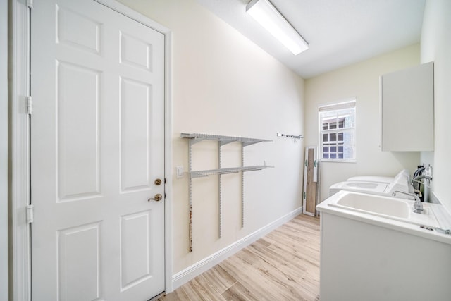 washroom with light wood finished floors, laundry area, a sink, washing machine and clothes dryer, and baseboards