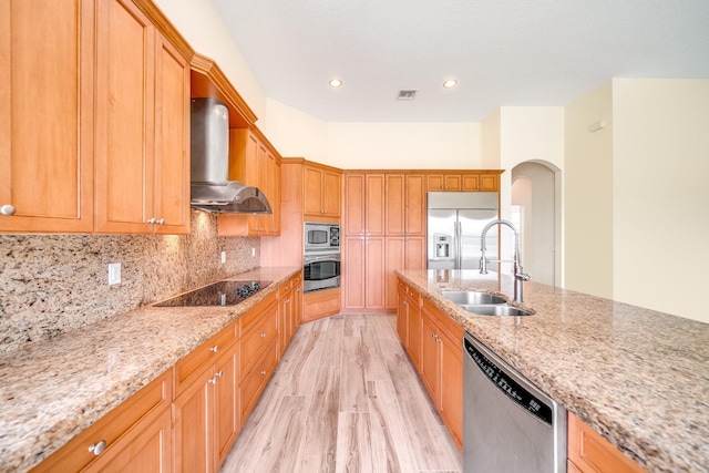 kitchen featuring wall chimney exhaust hood, arched walkways, a sink, visible vents, and built in appliances