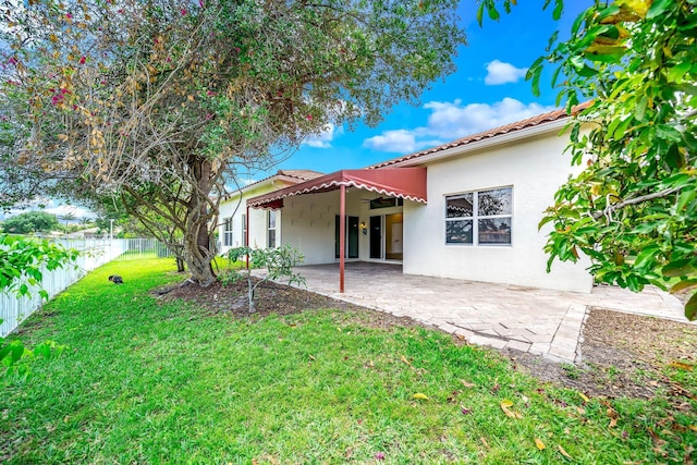 rear view of property with a lawn, a tiled roof, fence, a patio, and stucco siding