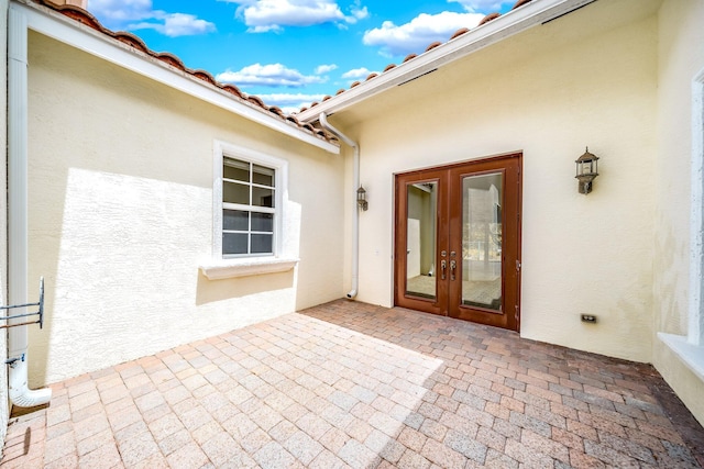 entrance to property with french doors, a tile roof, a patio, and stucco siding