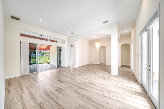 unfurnished living room featuring arched walkways, visible vents, and light wood-type flooring