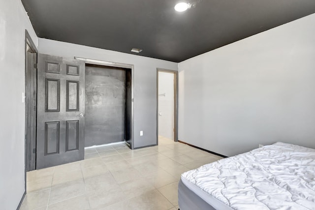 bedroom featuring a closet, light tile patterned floors, and baseboards