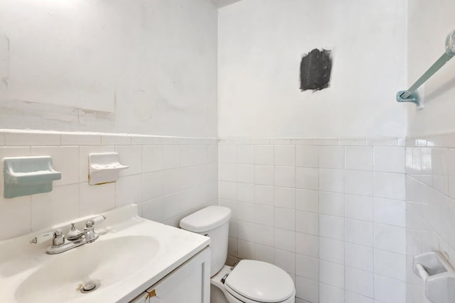half bathroom with toilet, vanity, wainscoting, and tile walls