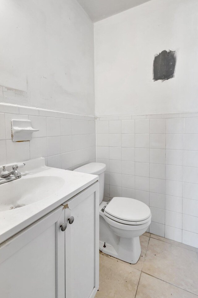 bathroom with vanity, tile patterned flooring, toilet, wainscoting, and tile walls