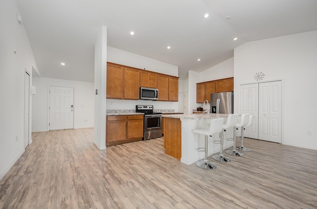 1544 Summit Rd SE, Palm Bay, FL 32909 - kitchen with brown cabinetry, appliances with stainless steel finishes, light wood finished floors, lofted ceiling, and a center island with sink