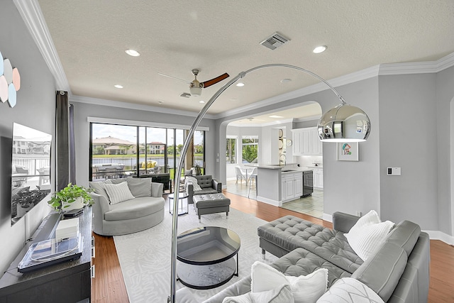living area with a textured ceiling, ceiling fan, light wood-style floors, and arched walkways