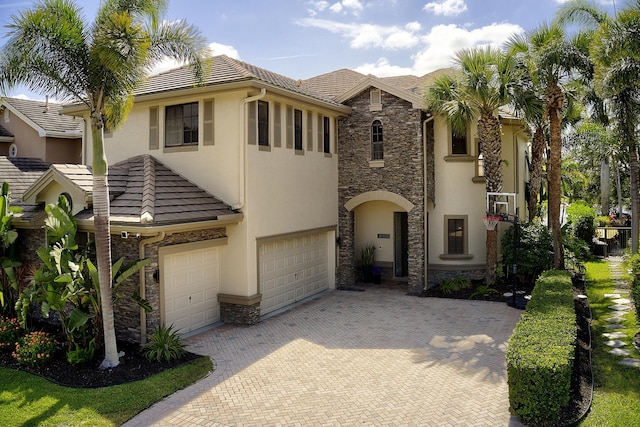 view of front of home featuring decorative driveway, stone siding, stucco siding, and a garage