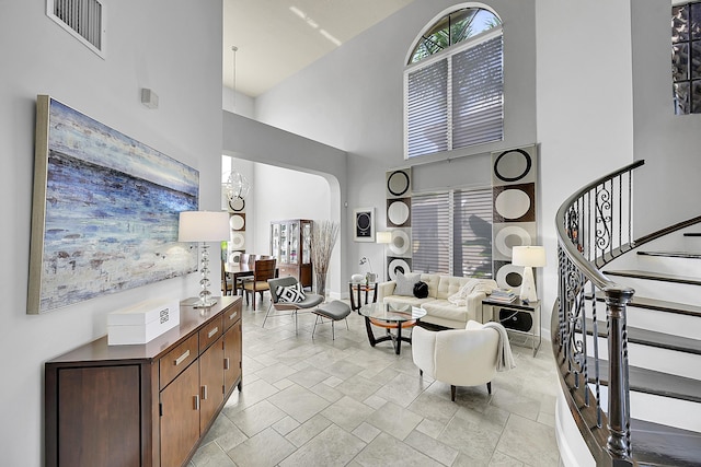 living area featuring stairway, visible vents, stone tile flooring, arched walkways, and a towering ceiling