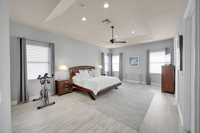 bedroom featuring visible vents, light wood-style floors, a tray ceiling, baseboards, and recessed lighting