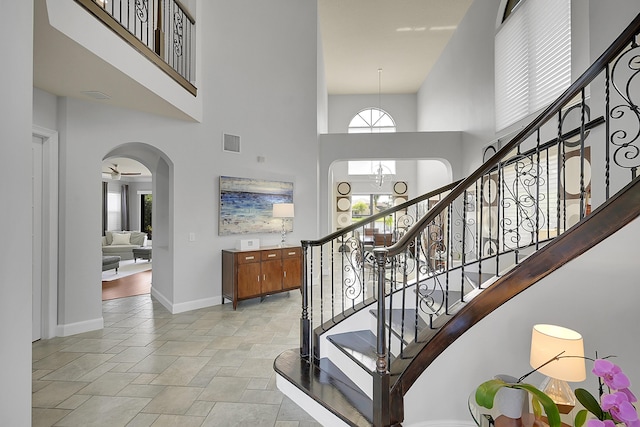 stairway featuring stone finish floor, visible vents, a towering ceiling, and arched walkways