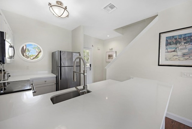 kitchen with a sink, stainless steel appliances, visible vents, baseboards, and dark wood finished floors
