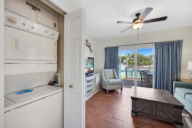 clothes washing area featuring stacked washer and clothes dryer, a ceiling fan, wood finished floors, and laundry area