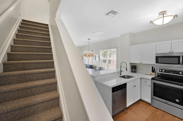 kitchen with white cabinets, a sink, visible vents, stainless steel appliances, and wood finished floors