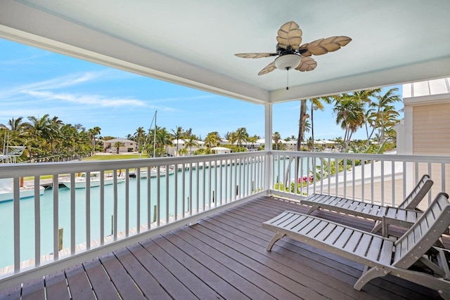 wooden deck with a ceiling fan, an outdoor pool, and a water view