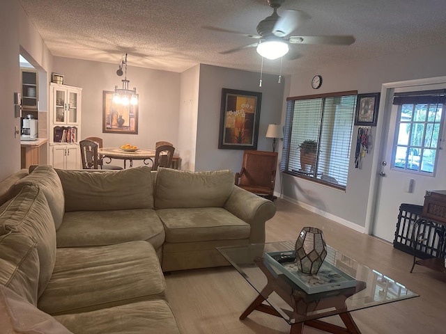 living area featuring a textured ceiling, light wood-type flooring, a ceiling fan, and baseboards