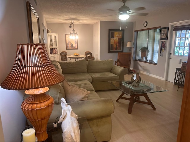 living area featuring a chandelier, a textured ceiling, light wood-type flooring, ceiling fan, and baseboards