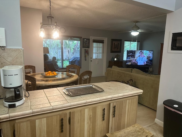 kitchen with light brown cabinets, a textured ceiling, a ceiling fan, open floor plan, and tile counters