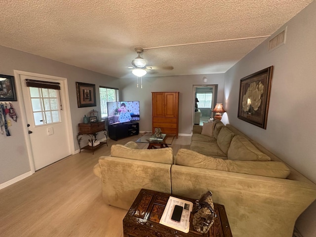 living area with light wood finished floors, a textured ceiling, plenty of natural light, a ceiling fan, and baseboards