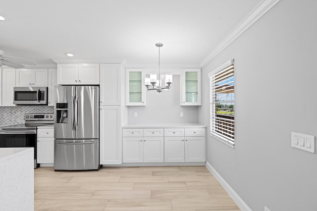 kitchen with glass insert cabinets, white cabinets, light countertops, appliances with stainless steel finishes, and crown molding