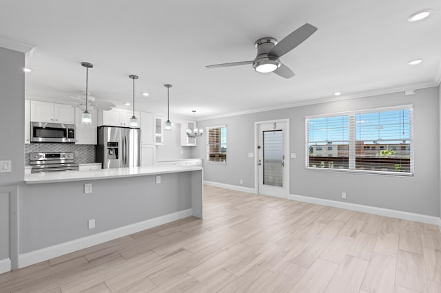 kitchen featuring ornamental molding, light countertops, white cabinetry, appliances with stainless steel finishes, and ceiling fan with notable chandelier