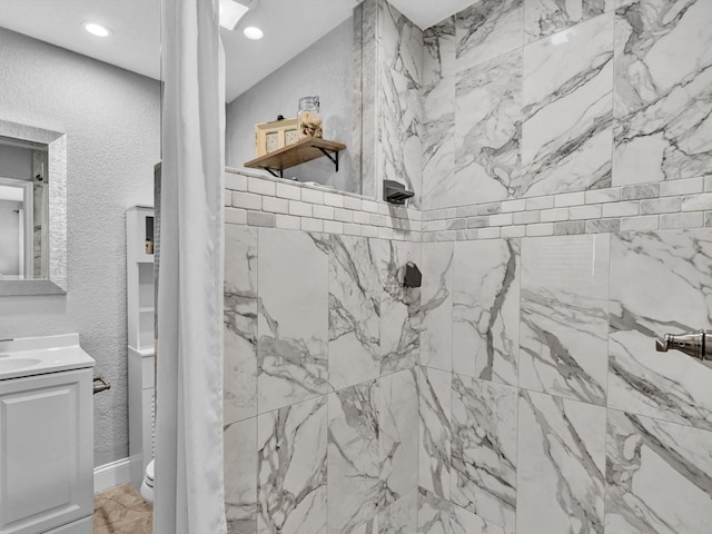 full bathroom featuring tiled shower, vanity, a textured wall, toilet, and recessed lighting