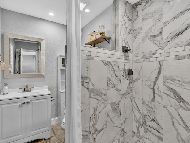 bathroom with toilet, a textured wall, vanity, and tiled shower