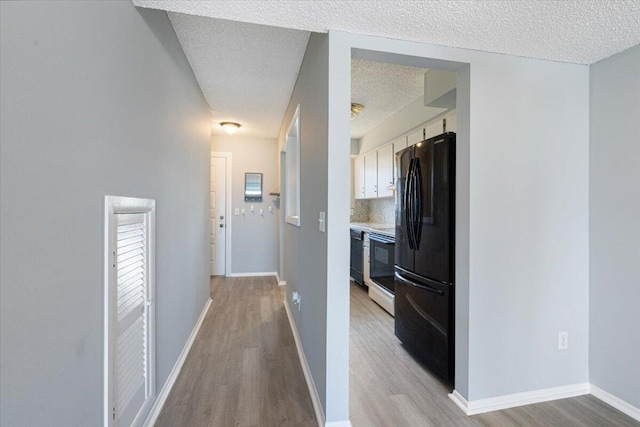 hall with baseboards, light wood-type flooring, and a textured ceiling