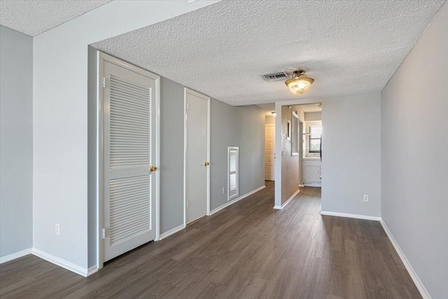 interior space with a textured ceiling, baseboards, wood finished floors, and visible vents