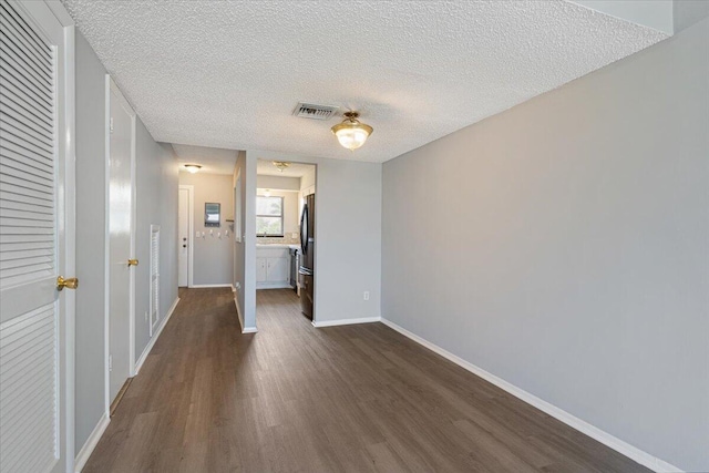 interior space with baseboards, a textured ceiling, dark wood-style floors, and visible vents